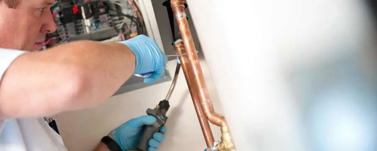 Water heater repair technician testing copper pipe connections and controls in Des Moines, IA