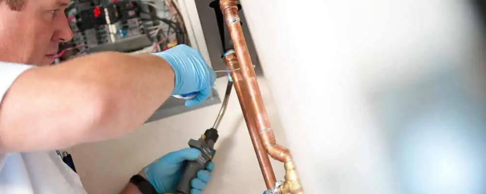 Water heater repair technician testing copper pipe connections and controls in Des Moines, IA